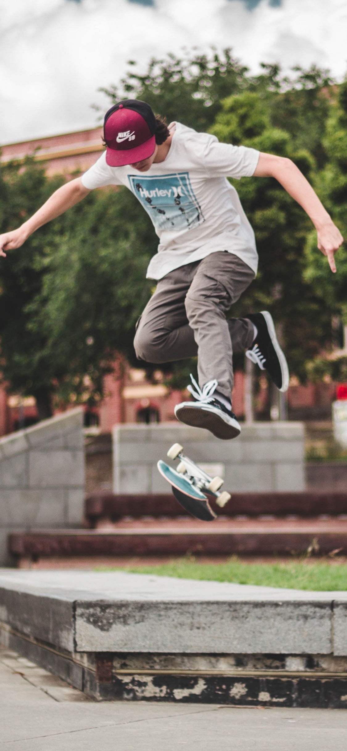 Man in Blue Shirt and Gray Pants Jumping on Brown Concrete Brick During Daytime. Wallpaper in 1125x2436 Resolution