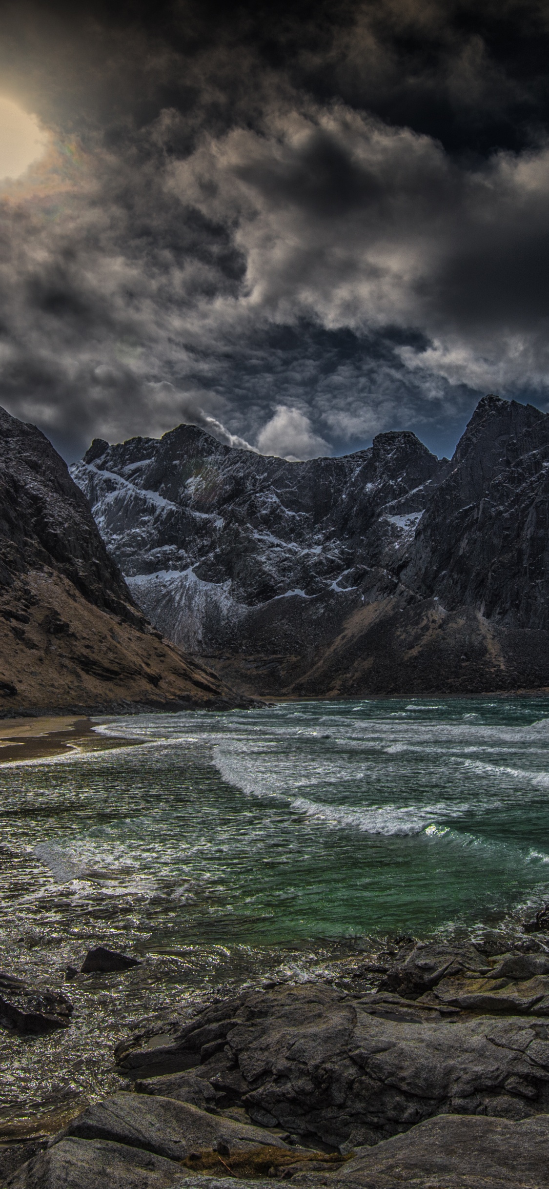 Brown Rocky Mountain Beside Body of Water Under Cloudy Sky During Daytime. Wallpaper in 1125x2436 Resolution