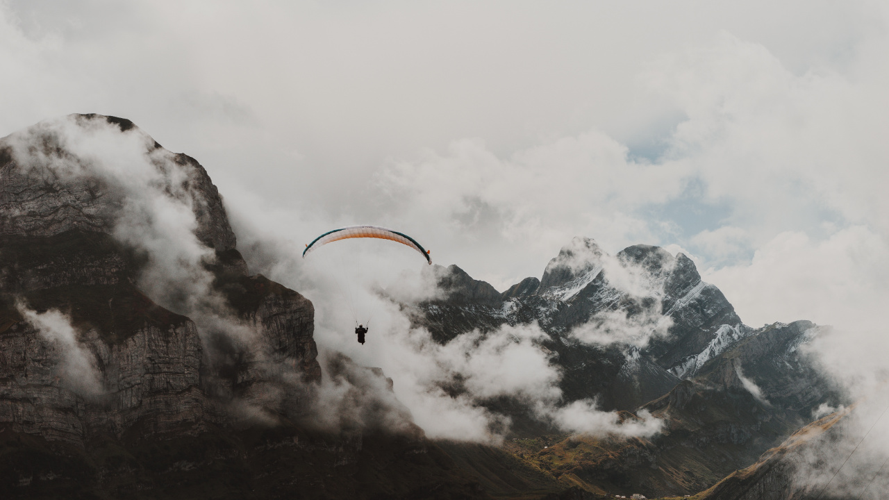 Person Riding Parachute Over Snow Covered Mountain. Wallpaper in 1280x720 Resolution