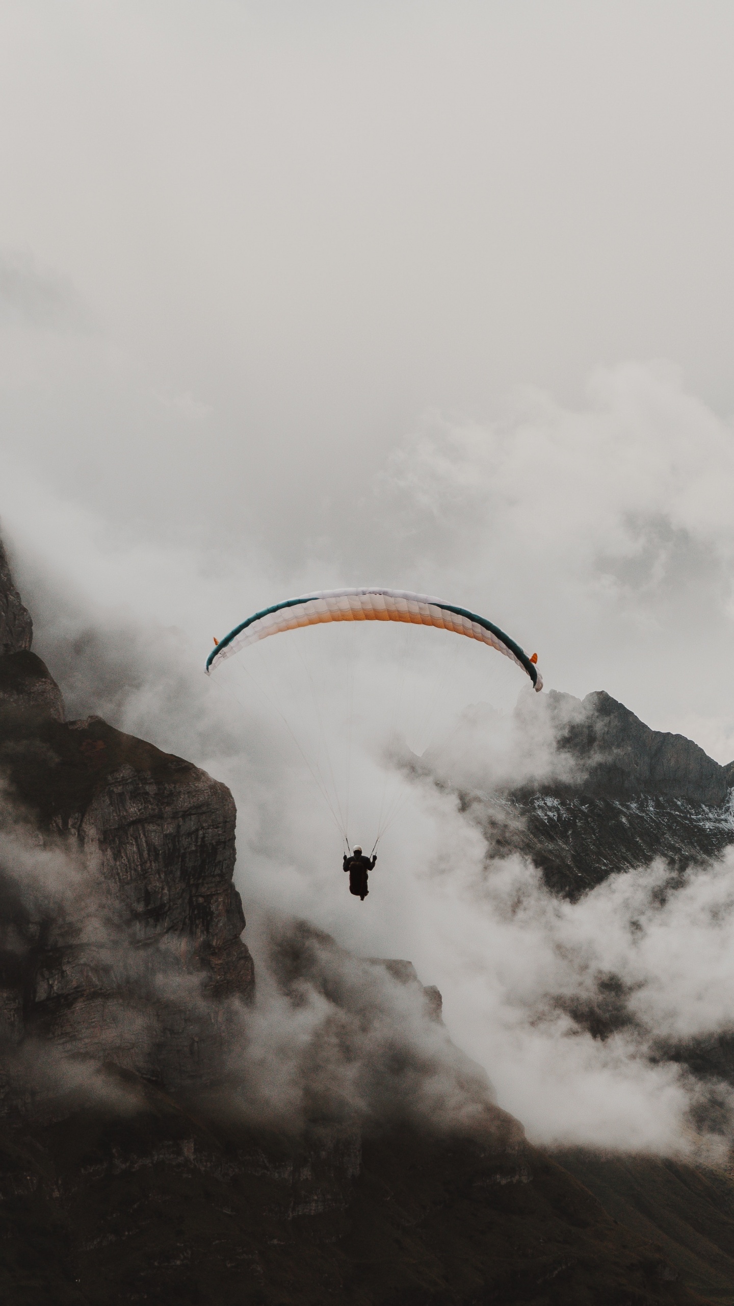 Person Riding Parachute Over Snow Covered Mountain. Wallpaper in 1440x2560 Resolution