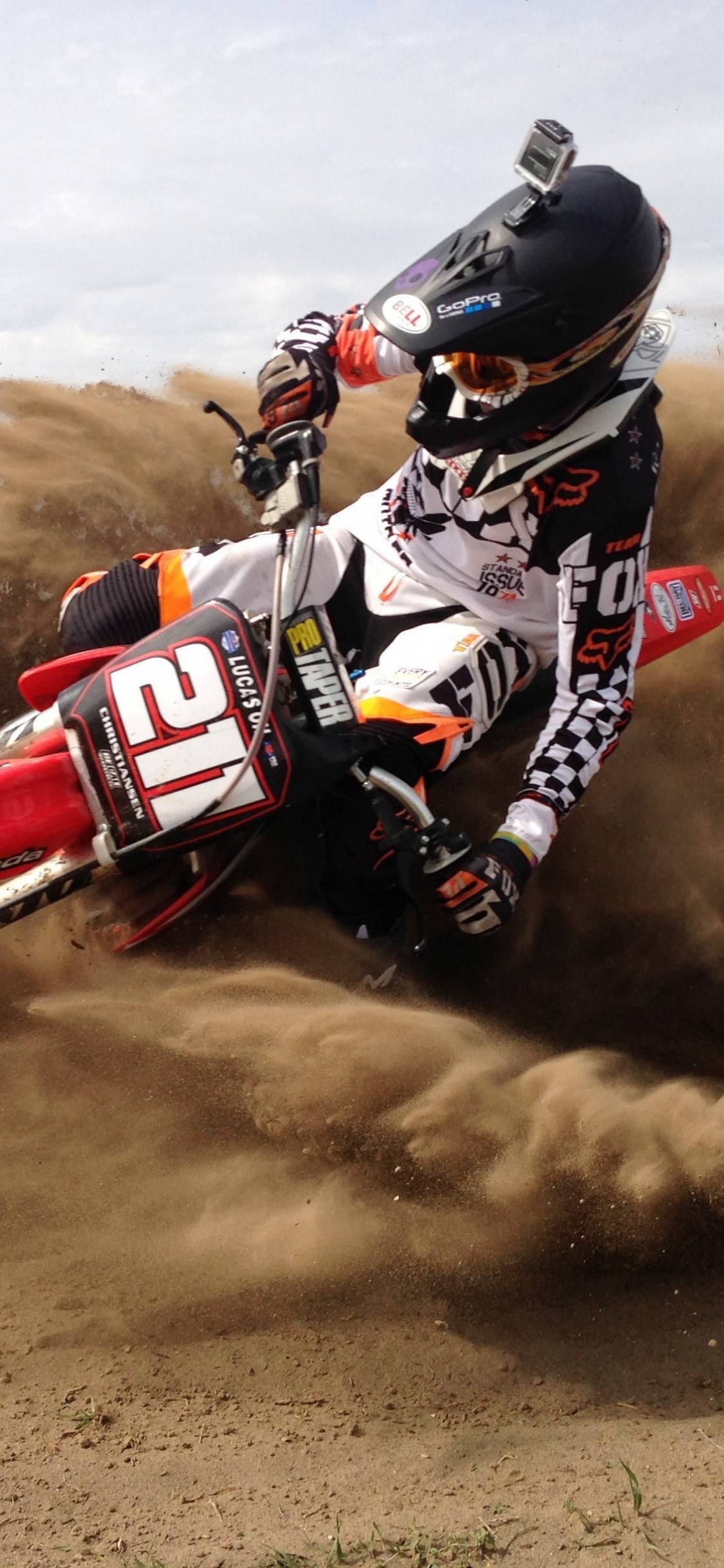 Mann, Der Tagsüber Rotes Und Weißes Motocross-Dirtbike Auf Braunem Sand Fährt. Wallpaper in 1125x2436 Resolution