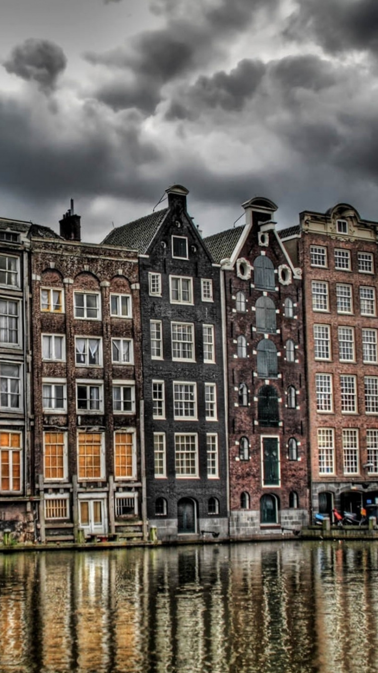 Brown and Black Concrete Building Near Body of Water Under Gray Clouds. Wallpaper in 750x1334 Resolution