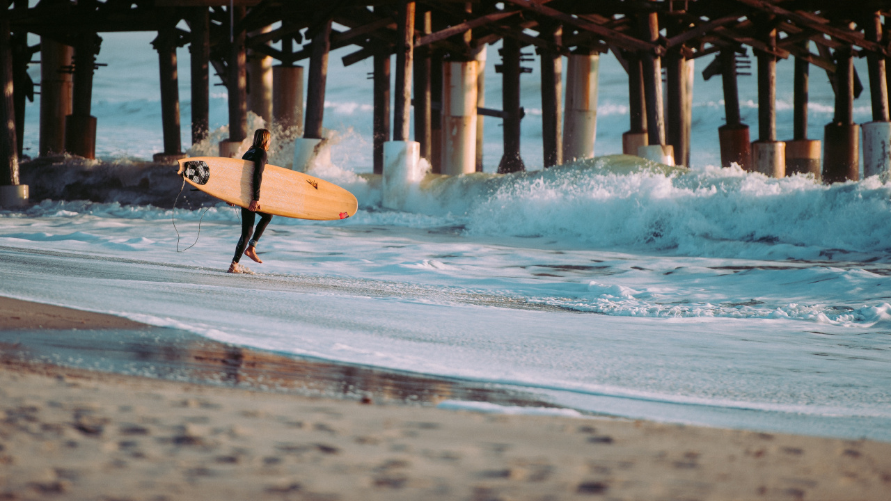 Persona Sosteniendo Una Tabla de Surf Blanca Caminando Por la Playa Durante el Día. Wallpaper in 1280x720 Resolution