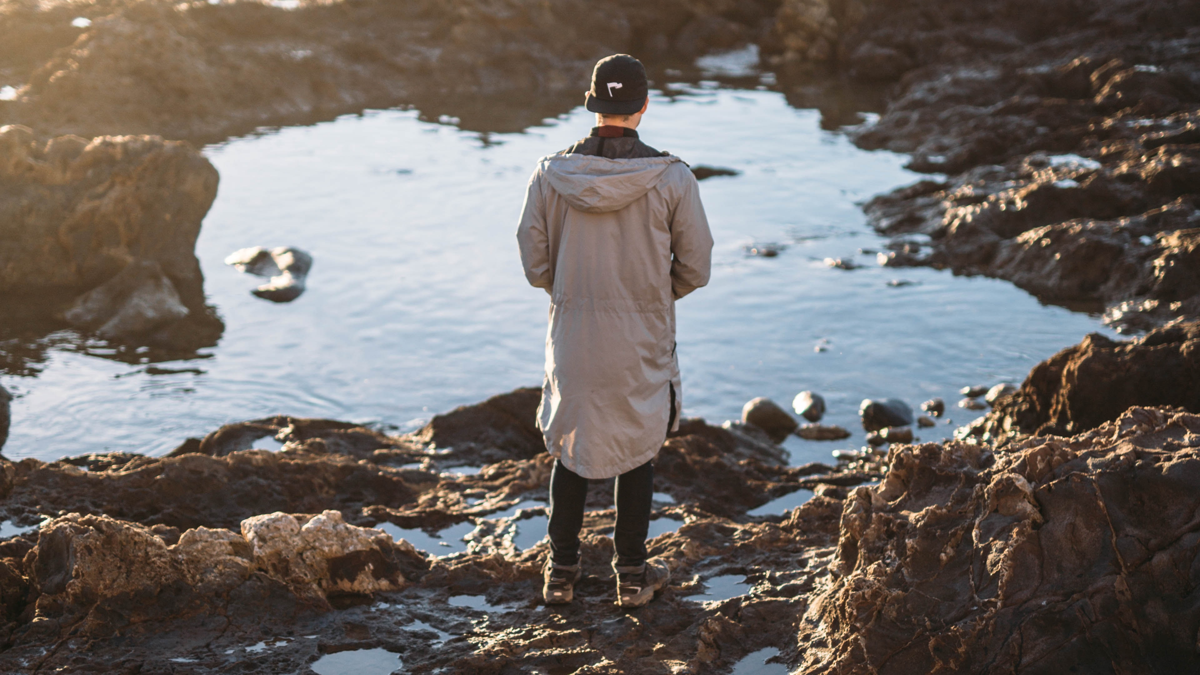 Man in White Jacket Standing on Rock Near Body of Water During Daytime. Wallpaper in 3840x2160 Resolution