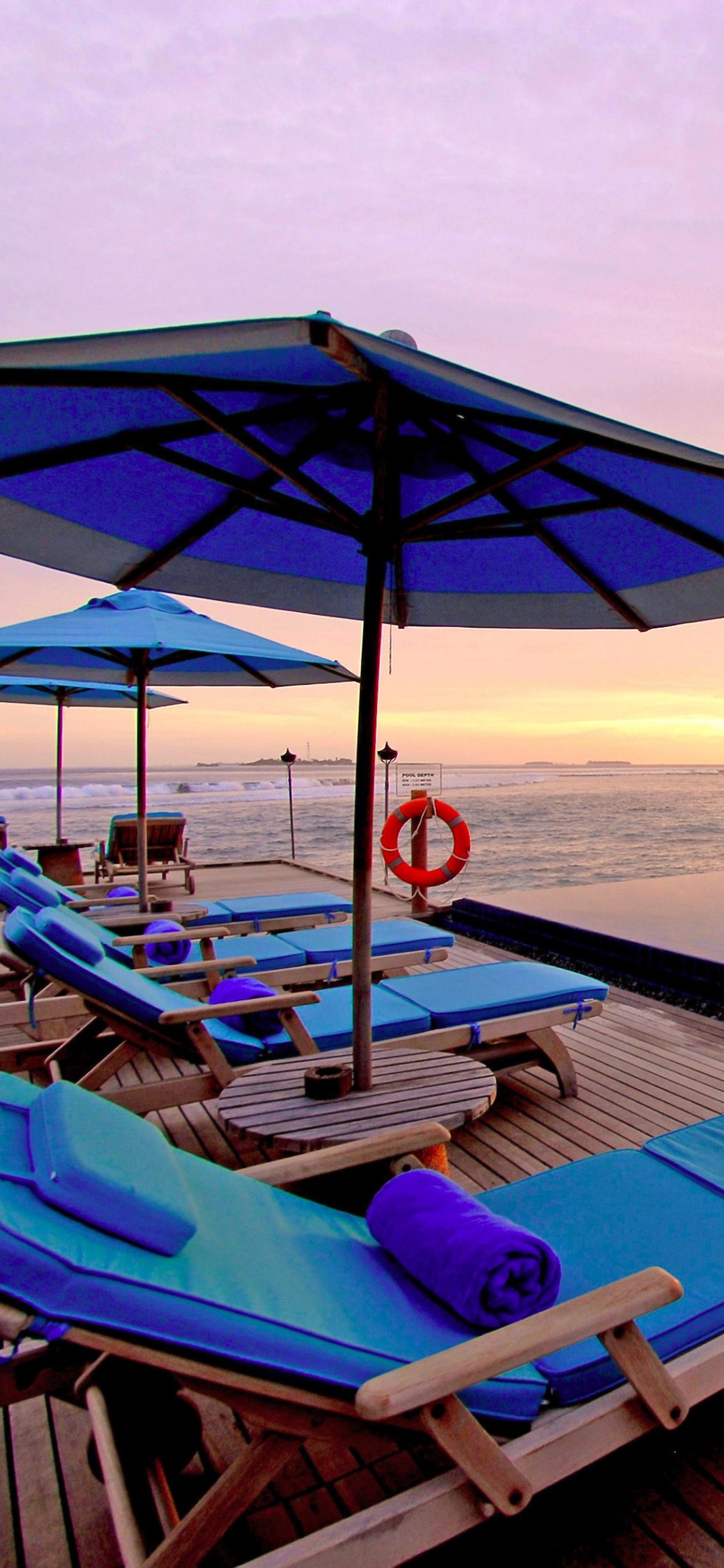 Blue and White Lounge Chairs on Beach During Sunset. Wallpaper in 1125x2436 Resolution