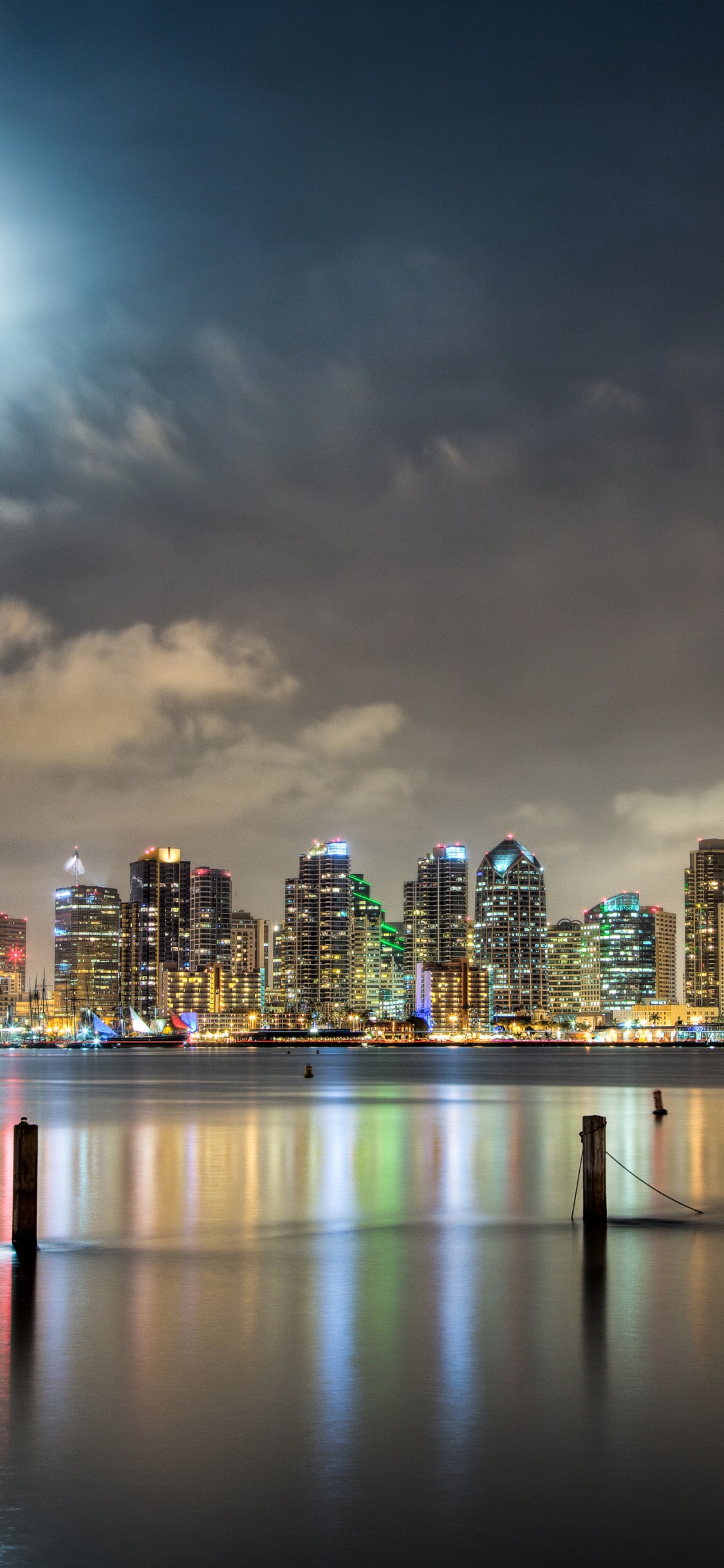 Skyline Der Stadt Über Gewässer Während Der Nacht. Wallpaper in 1125x2436 Resolution