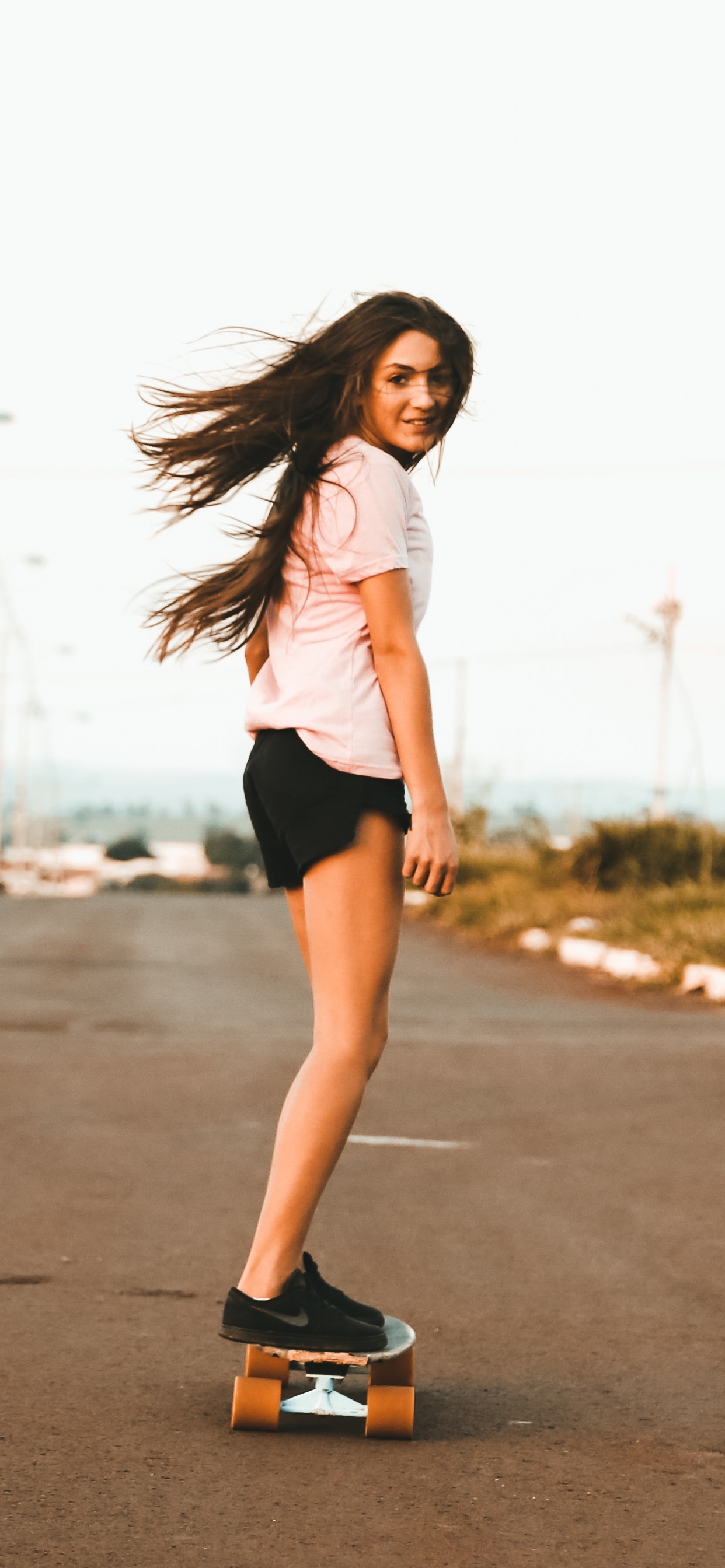 Woman in White Tank Top and Black Shorts Standing on Road During Daytime. Wallpaper in 1242x2688 Resolution