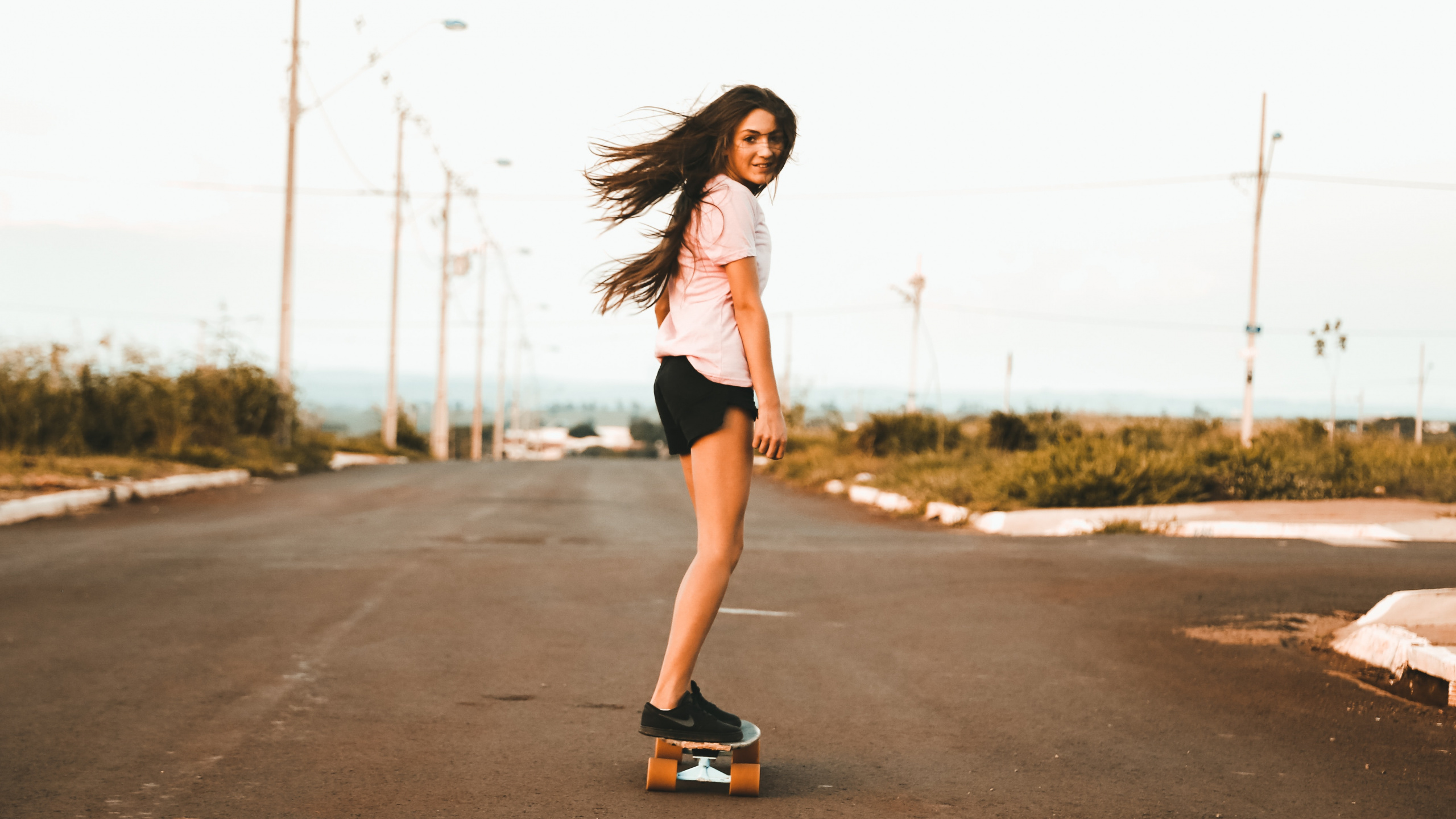 Woman in White Tank Top and Black Shorts Standing on Road During Daytime. Wallpaper in 2560x1440 Resolution