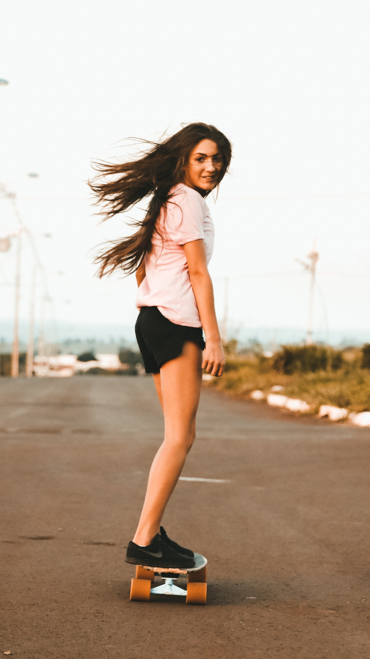 Woman in White Tank Top and Black Shorts Standing on Road During Daytime. Wallpaper in 750x1334 Resolution