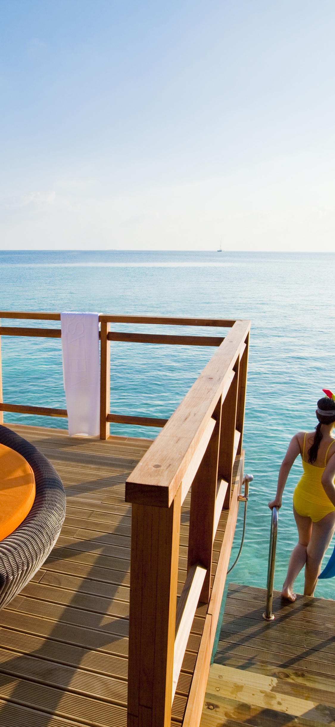 Woman in Blue Bikini Sitting on Brown Wooden Bench Near Sea During Daytime. Wallpaper in 1125x2436 Resolution