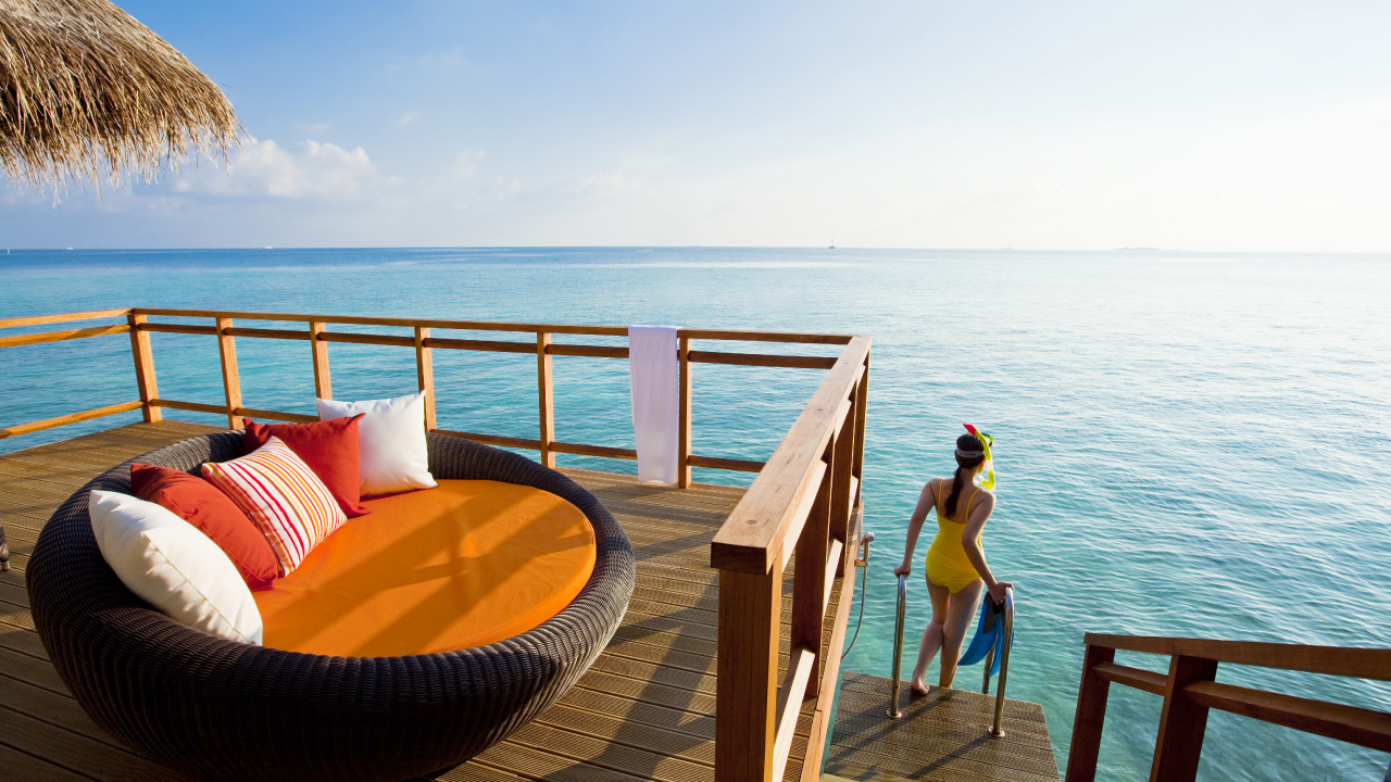 Woman in Blue Bikini Sitting on Brown Wooden Bench Near Sea During Daytime. Wallpaper in 1280x720 Resolution