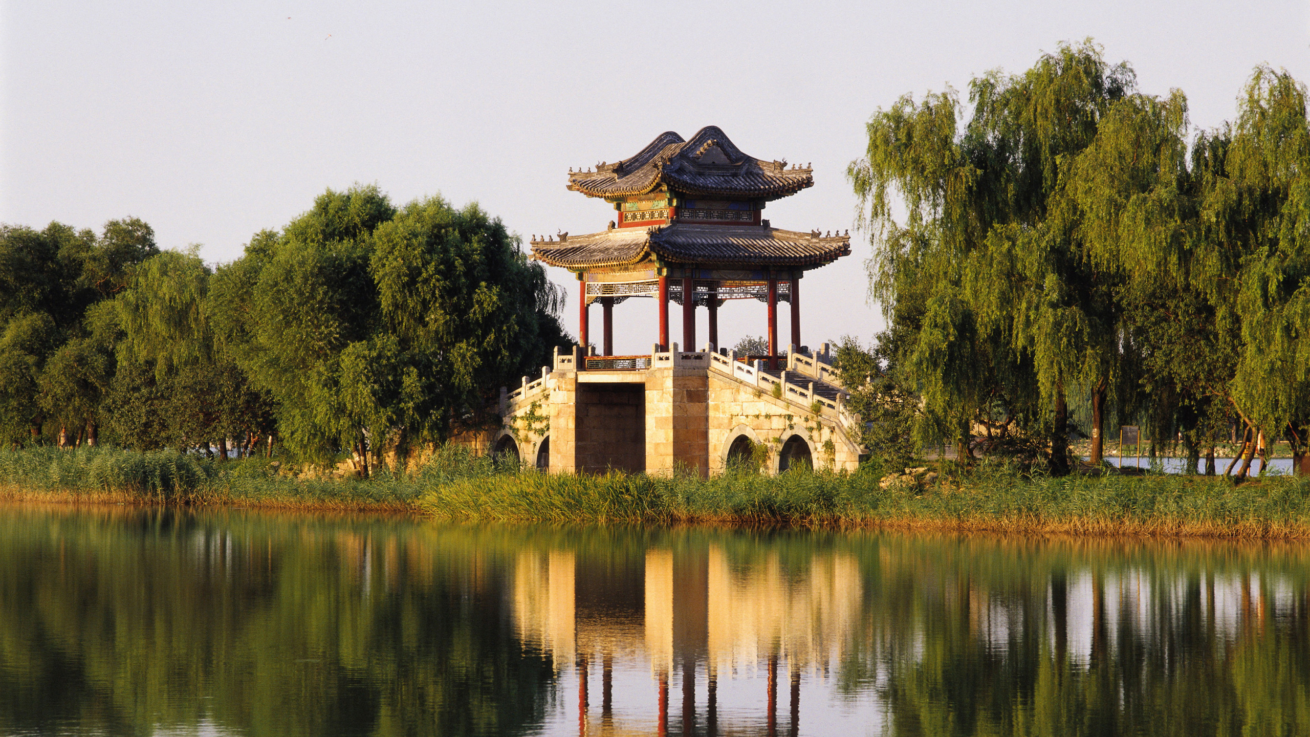 Edificio de Hormigón Marrón y Negro Cerca de Árboles Verdes y Lago Durante el Día. Wallpaper in 2560x1440 Resolution