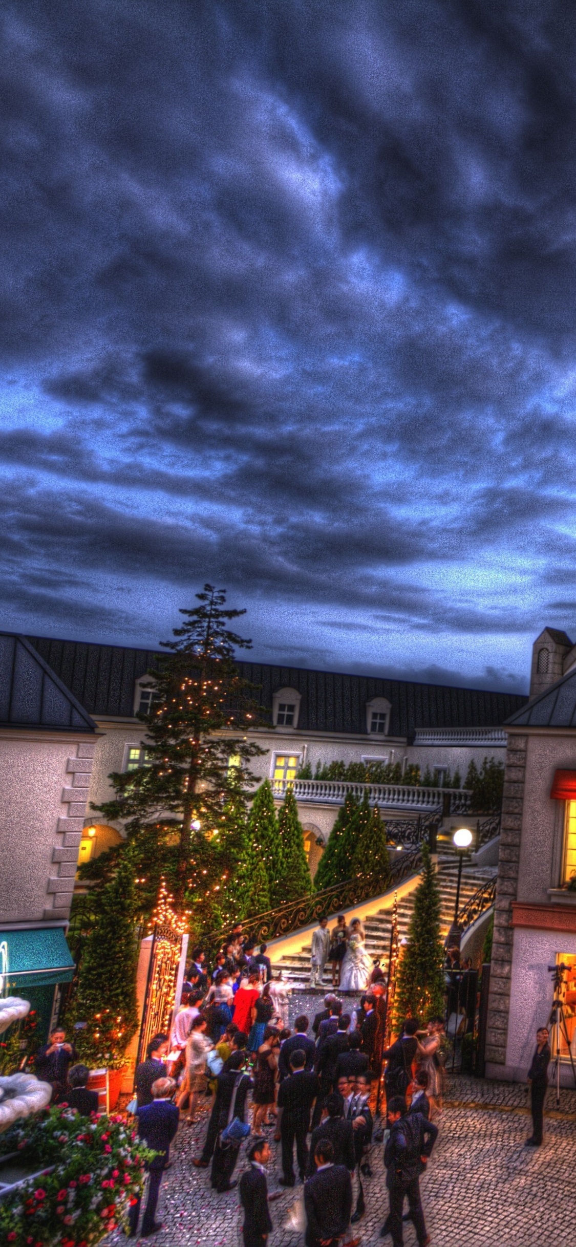 Gente Caminando en la Calle Cerca Del Edificio Durante la Noche. Wallpaper in 1125x2436 Resolution