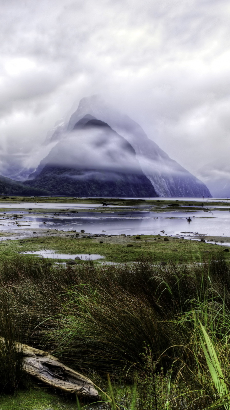 Green Grass Field Near Body of Water and Mountain Under White Clouds During Daytime. Wallpaper in 750x1334 Resolution