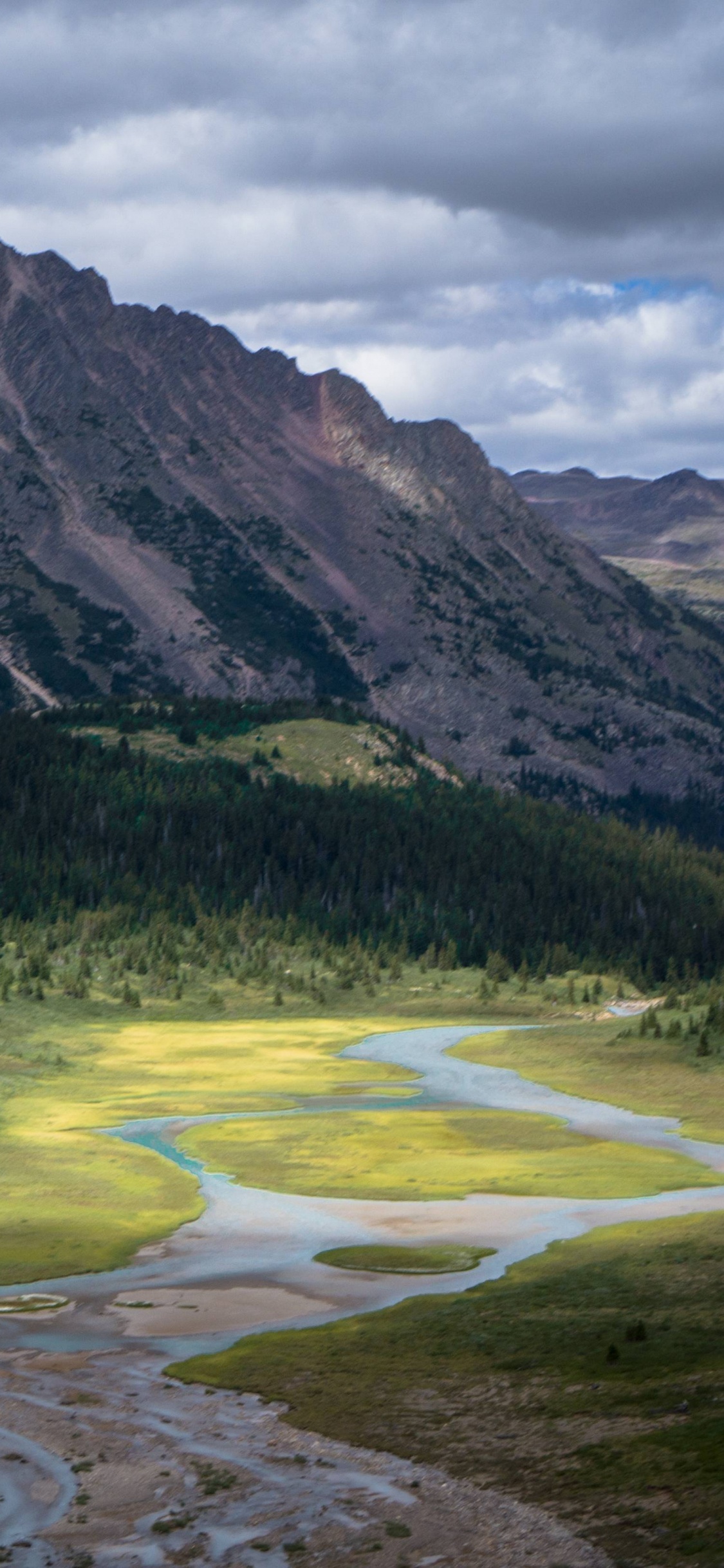 Green Grass Field Near Mountain Under Cloudy Sky During Daytime. Wallpaper in 1125x2436 Resolution