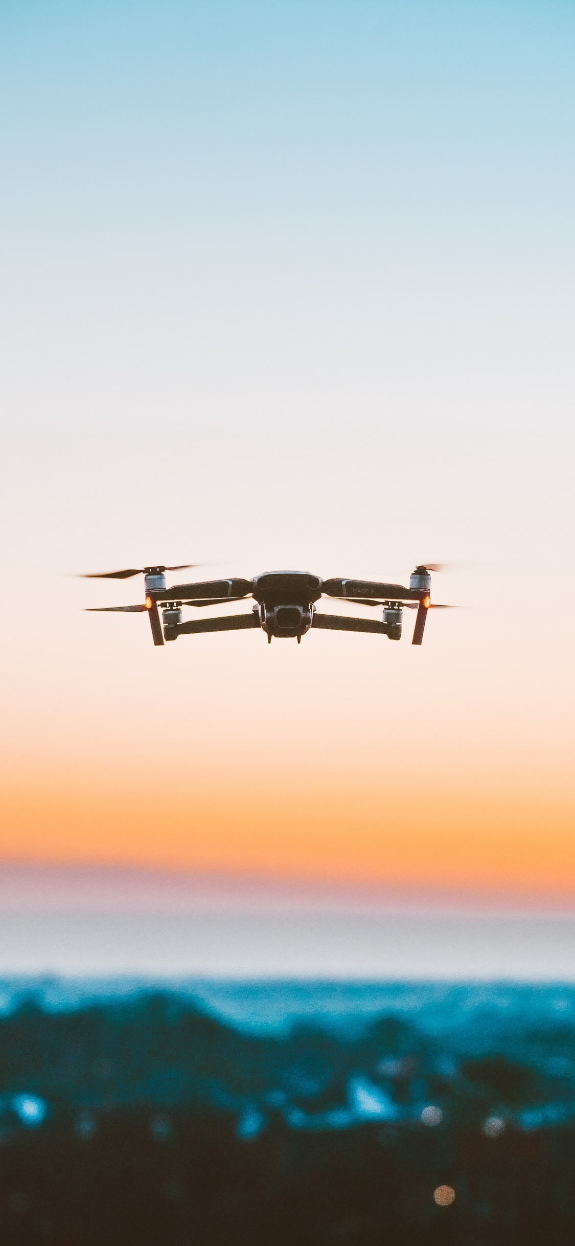 Schwarze Drohne, Die Bei Sonnenuntergang Über Das Meer Fliegt. Wallpaper in 1125x2436 Resolution