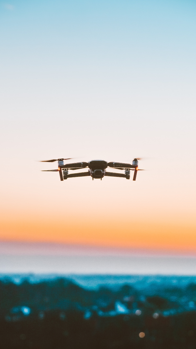 Schwarze Drohne, Die Bei Sonnenuntergang Über Das Meer Fliegt. Wallpaper in 750x1334 Resolution