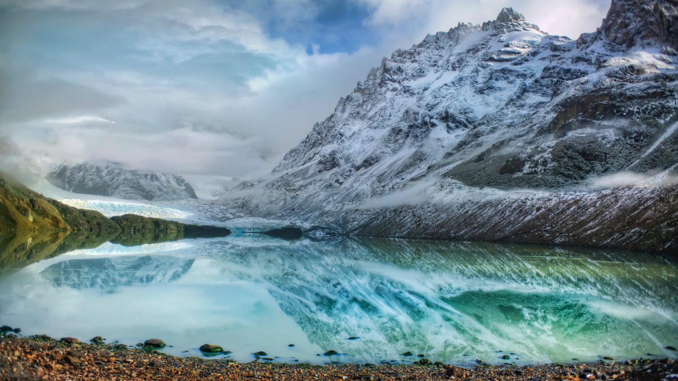 Snow Covered Mountain Near Body of Water Under Cloudy Sky During Daytime. Wallpaper in 1366x768 Resolution