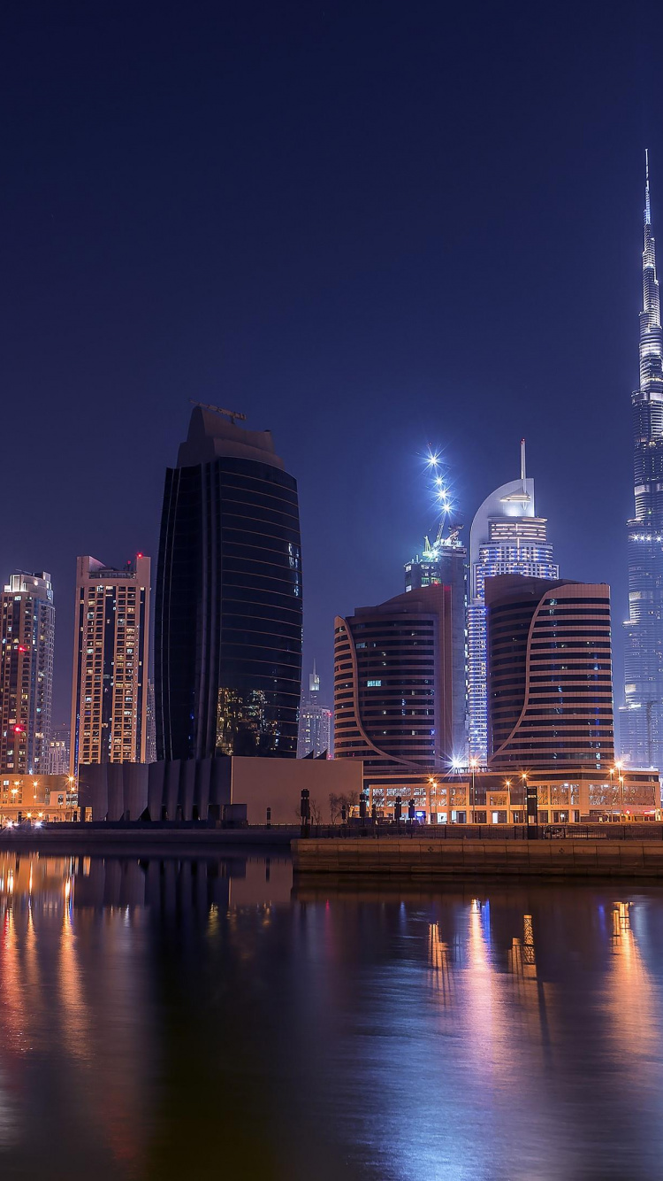 Skyline Der Stadt Über Gewässer Während Der Nacht. Wallpaper in 750x1334 Resolution
