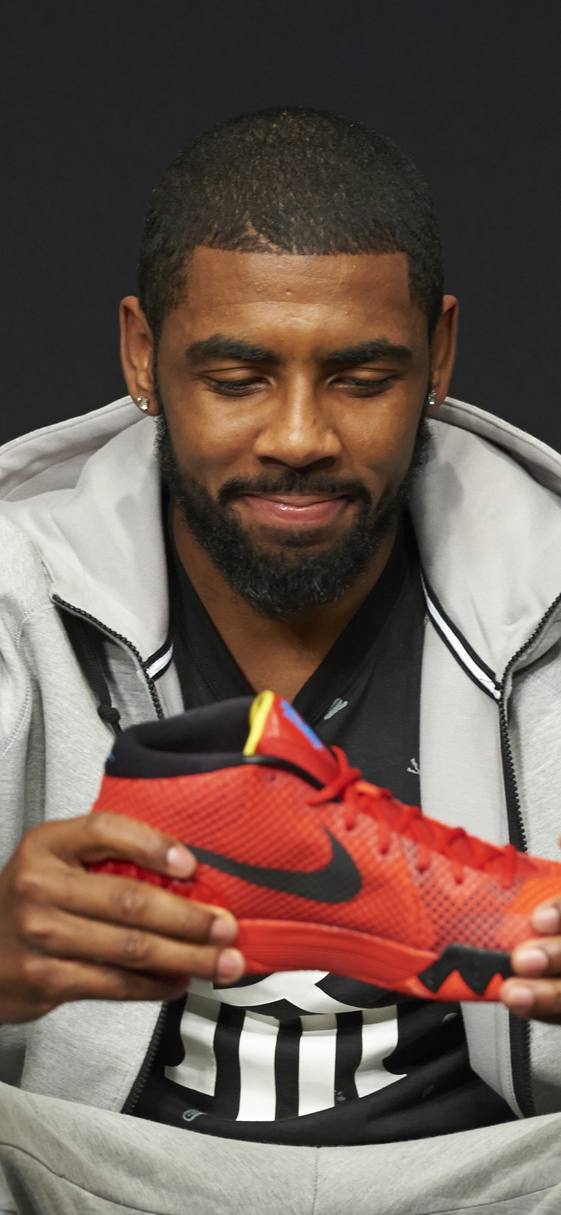 Hombre Con Camisa de Vestir Gris Sosteniendo Zapatillas Deportivas Nike Naranja. Wallpaper in 1125x2436 Resolution