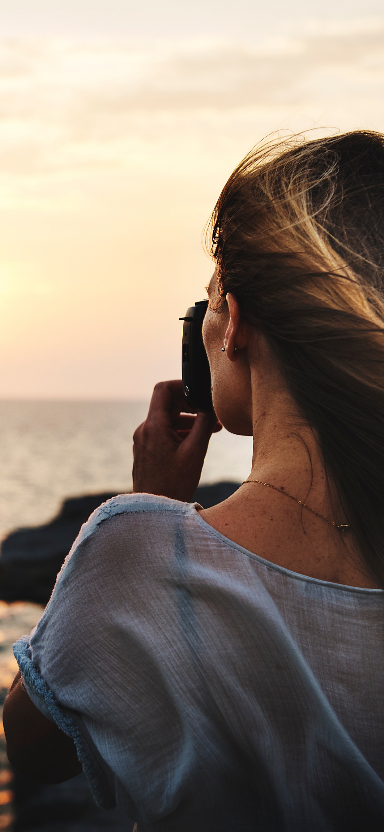 Femme en Chemise Blanche Prenant Une Photo de la Mer Pendant la Journée. Wallpaper in 1242x2688 Resolution