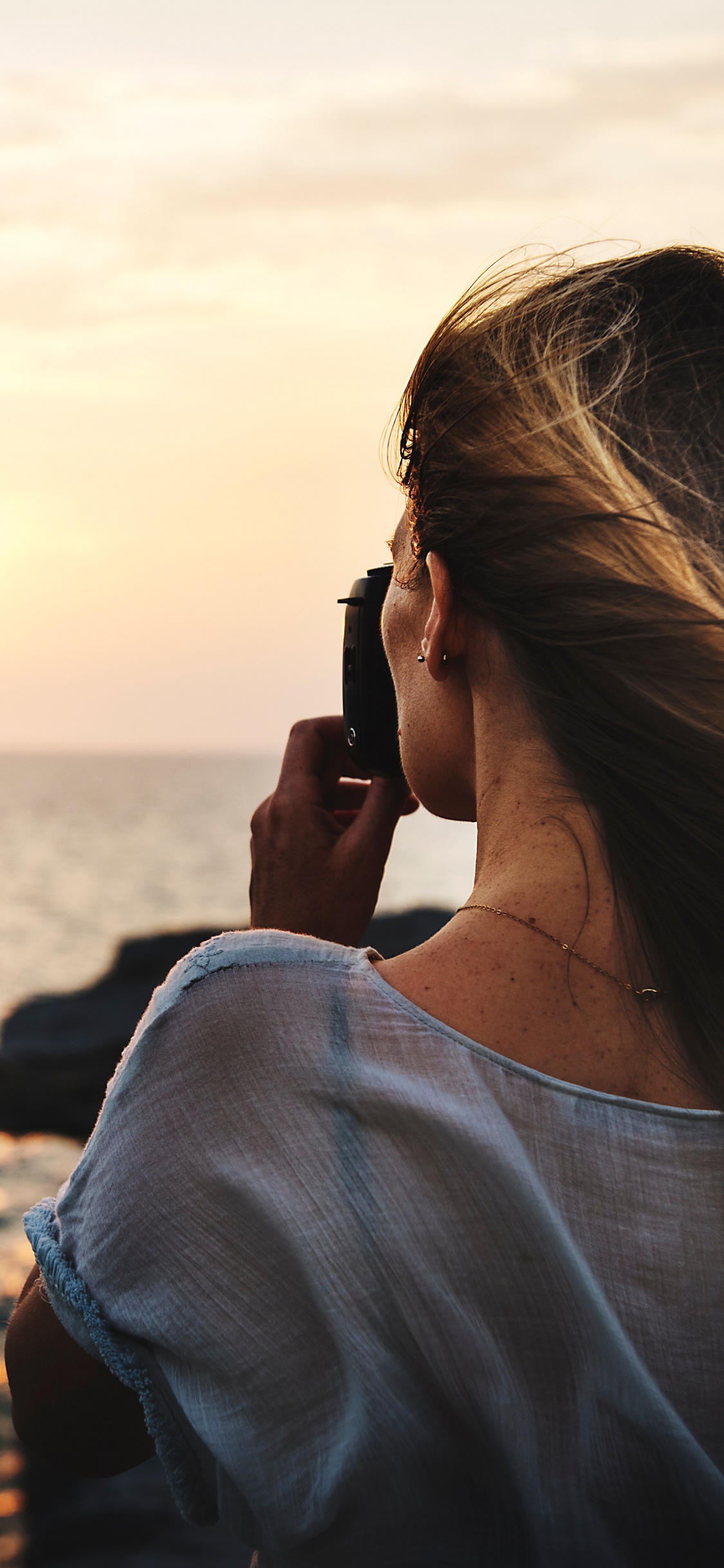 Woman in White Shirt Taking Photo of Sea During Daytime. Wallpaper in 1125x2436 Resolution
