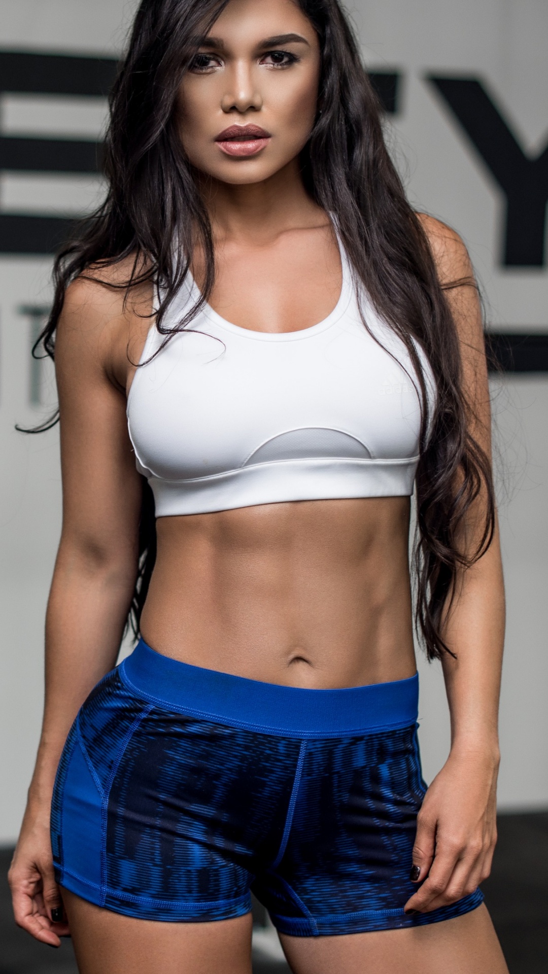 Woman in White Sports Bra and Blue Denim Shorts Standing Near White Wall. Wallpaper in 1080x1920 Resolution