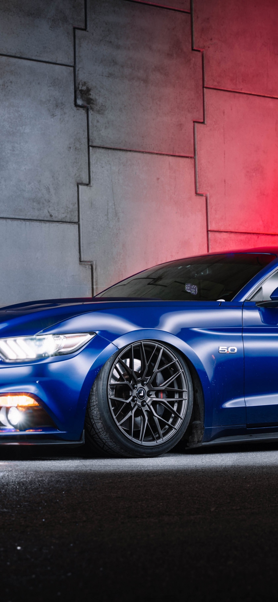 Blue Porsche 911 Parked Beside Red Wall. Wallpaper in 1125x2436 Resolution