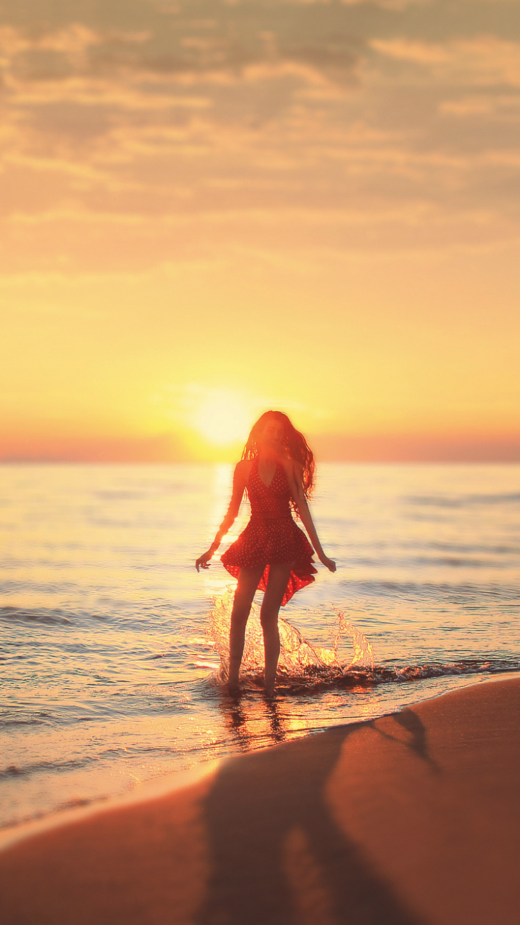 Mujer en Vestido Rojo Caminando Por la Playa Durante la Puesta de Sol. Wallpaper in 750x1334 Resolution