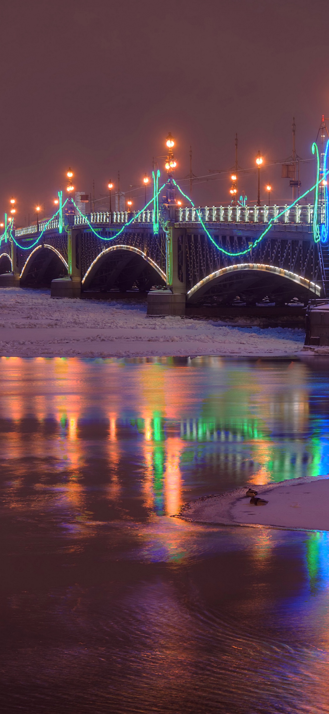 Blue Bridge Over Water During Night Time. Wallpaper in 1125x2436 Resolution