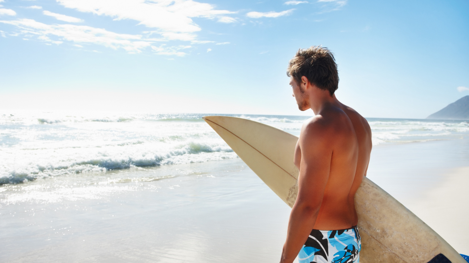 Man in Blue and White Board Shorts Holding White Surfboard on Beach During Daytime. Wallpaper in 1920x1080 Resolution
