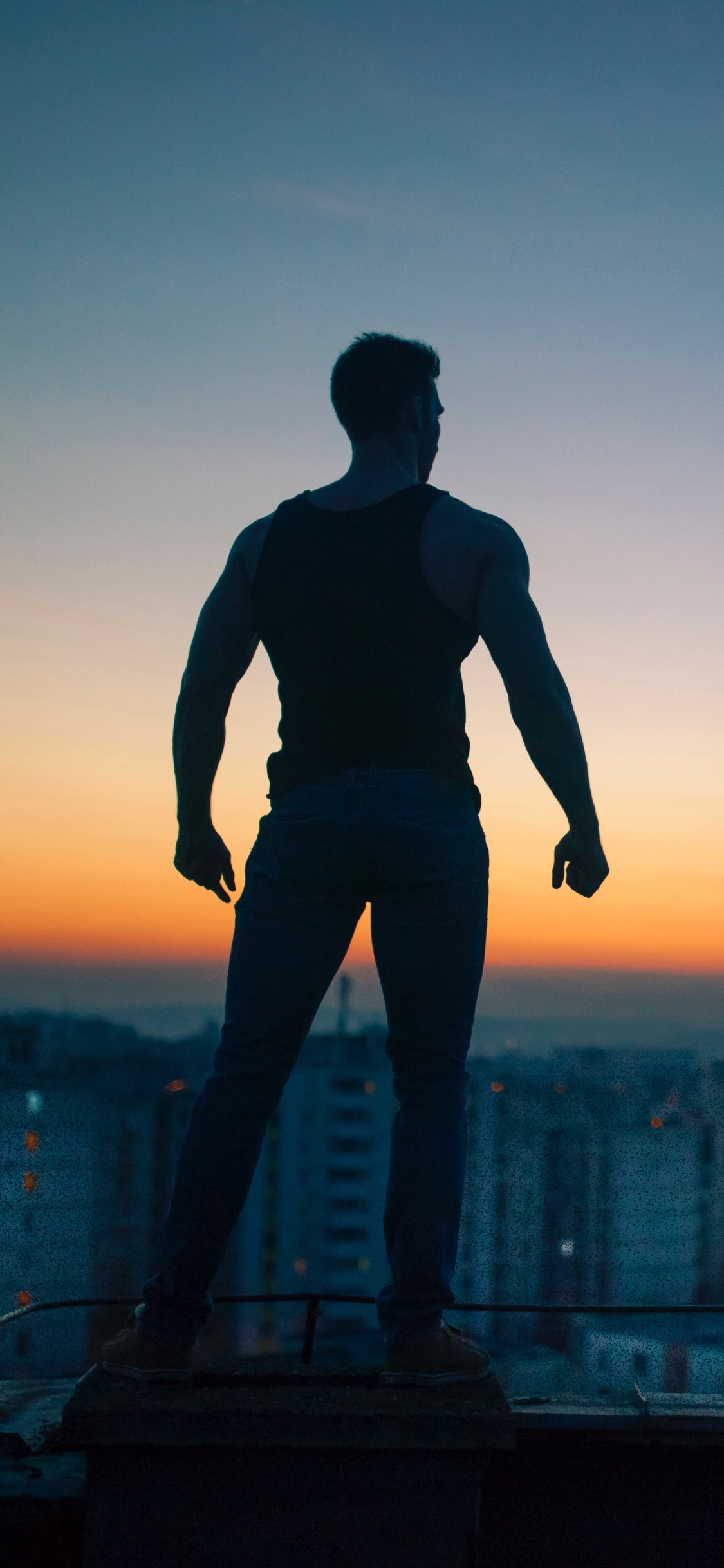 Mann in Schwarzem Hemd Und Hose, Der Während Des Sonnenuntergangs Auf Dem Gebäude Steht. Wallpaper in 1125x2436 Resolution