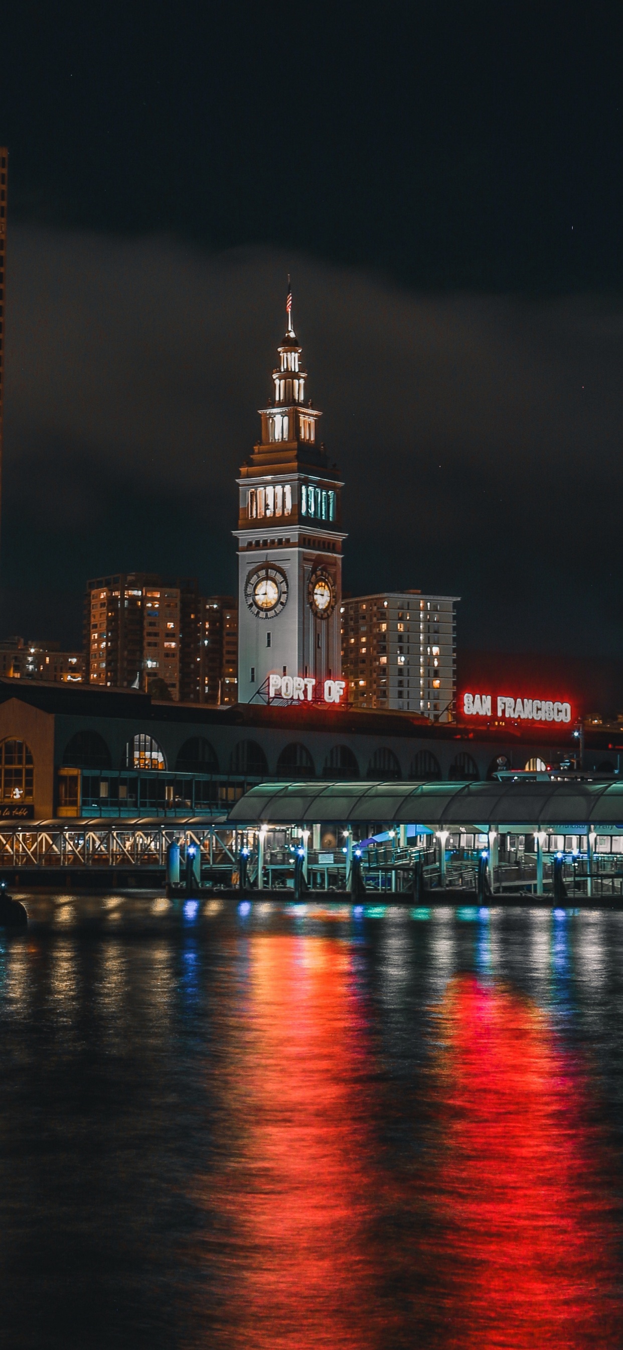 Lighted City Buildings Near Body of Water During Night Time. Wallpaper in 1242x2688 Resolution