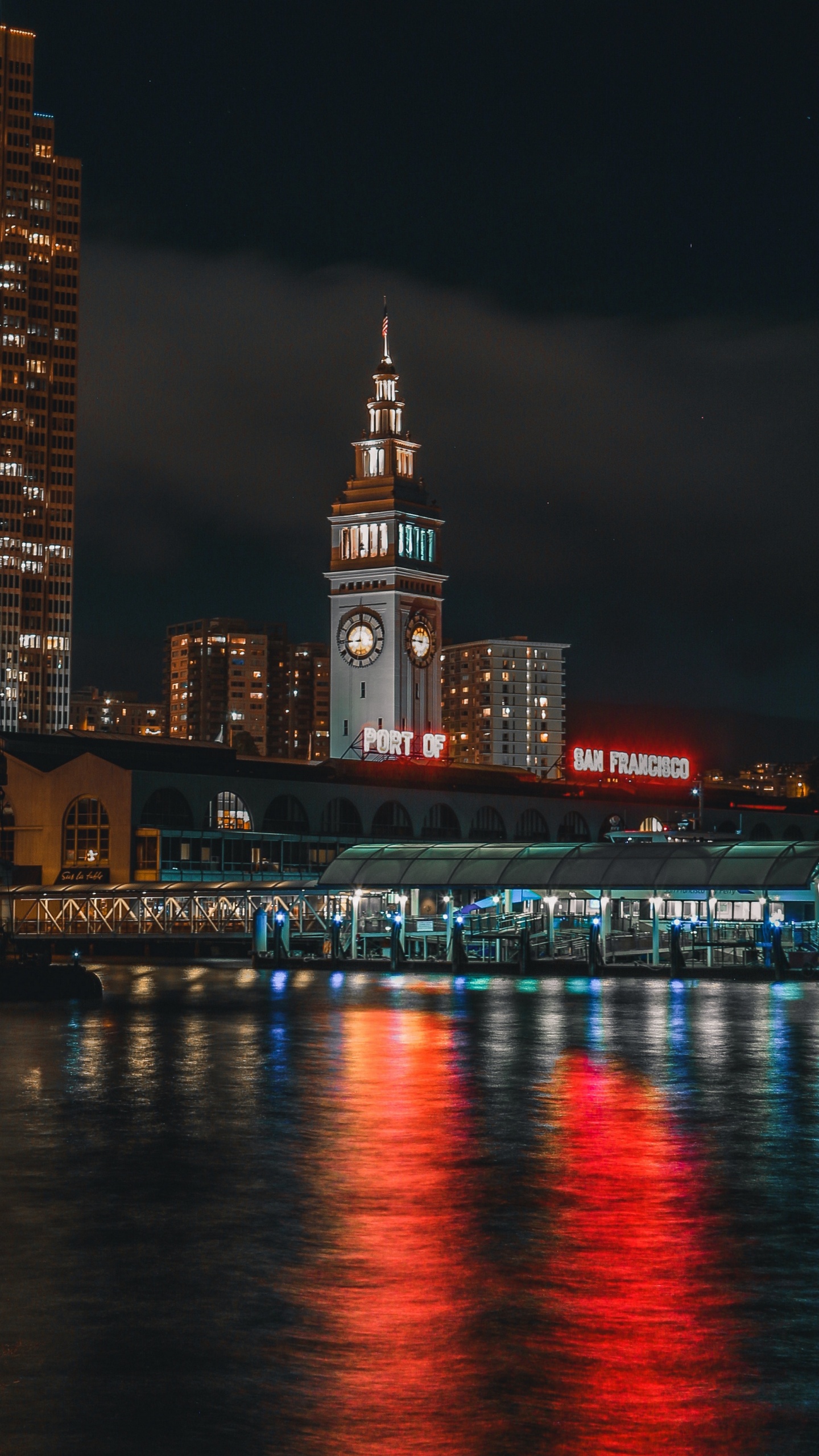 Lighted City Buildings Near Body of Water During Night Time. Wallpaper in 1440x2560 Resolution