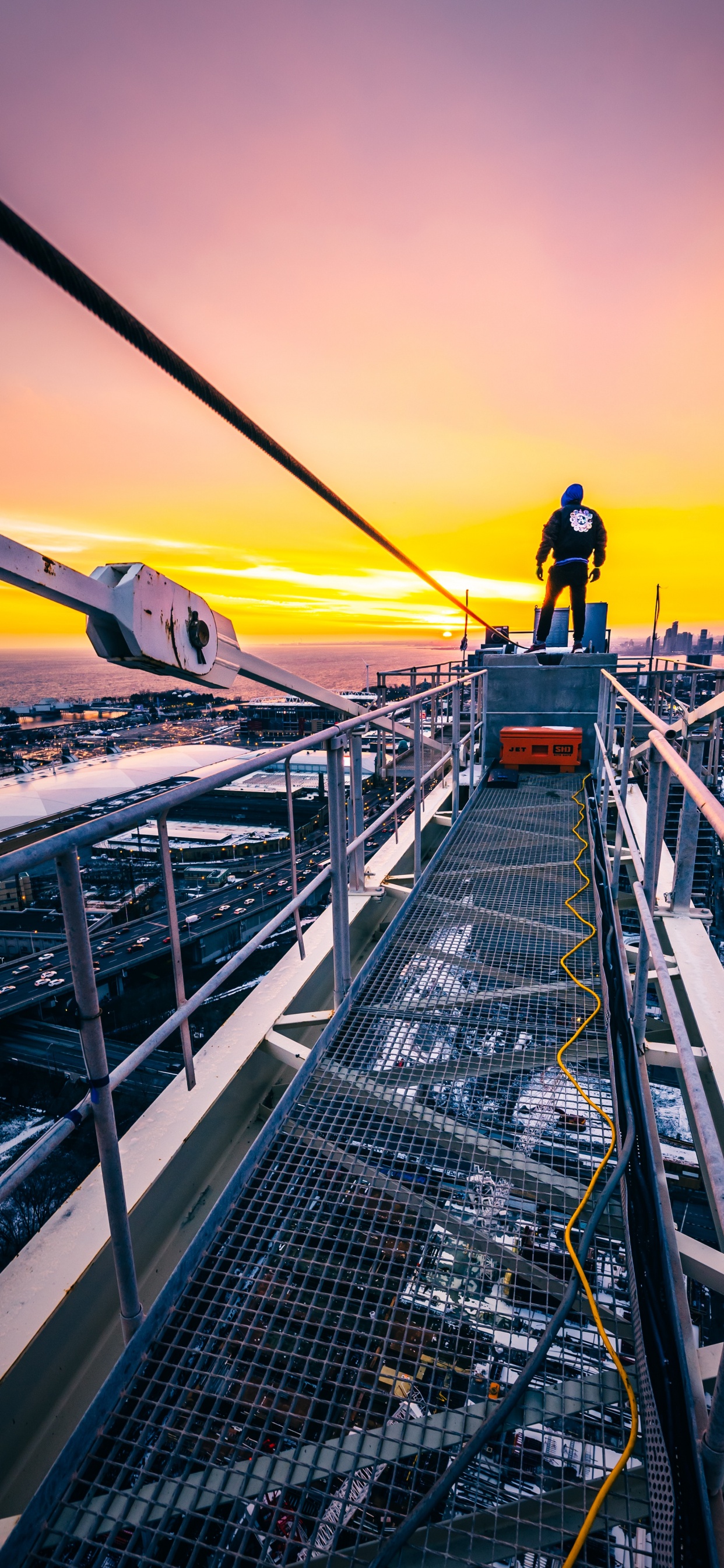 Hombre Con Chaqueta Negra y Pantalón Negro de Pie en la Parte Superior Del Edificio Durante la Puesta de Sol. Wallpaper in 1242x2688 Resolution