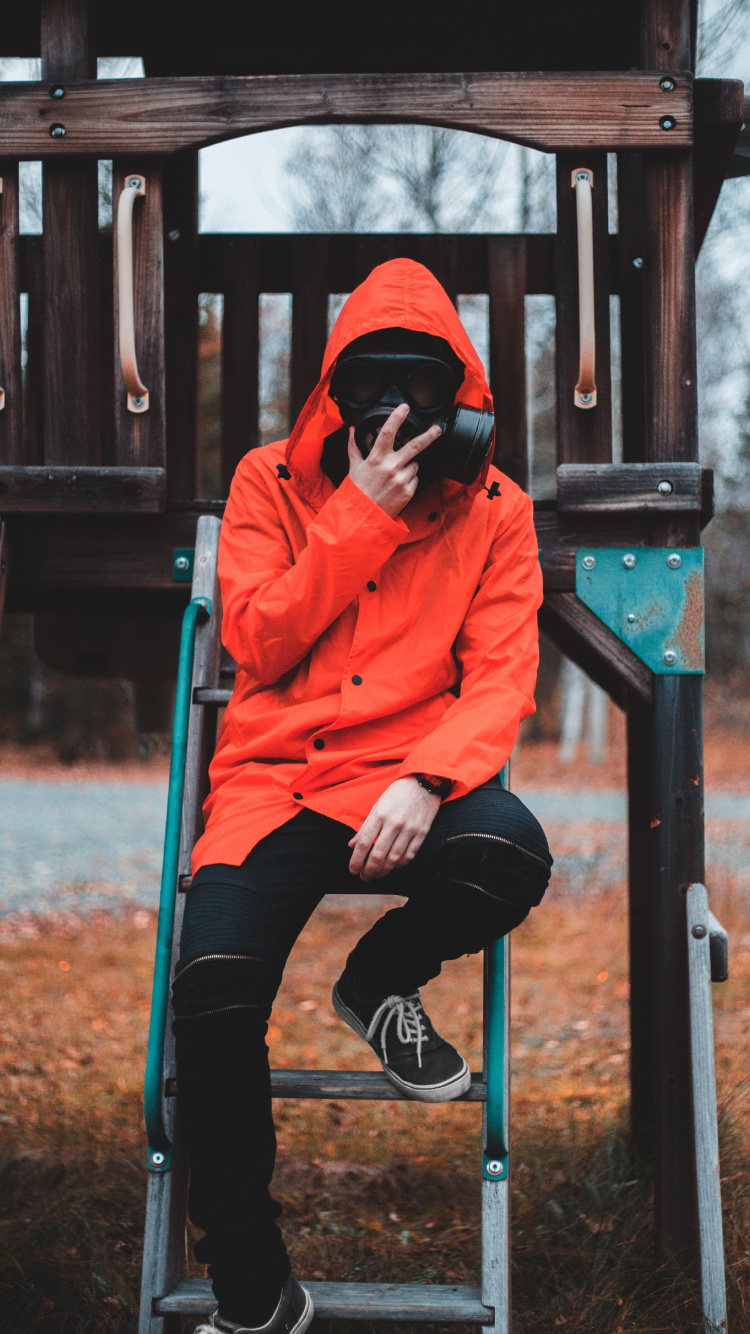 Frau in Orangefarbenem Hoodie Und Schwarzer Hose Sitzt Auf Braunem Holzzaun. Wallpaper in 750x1334 Resolution