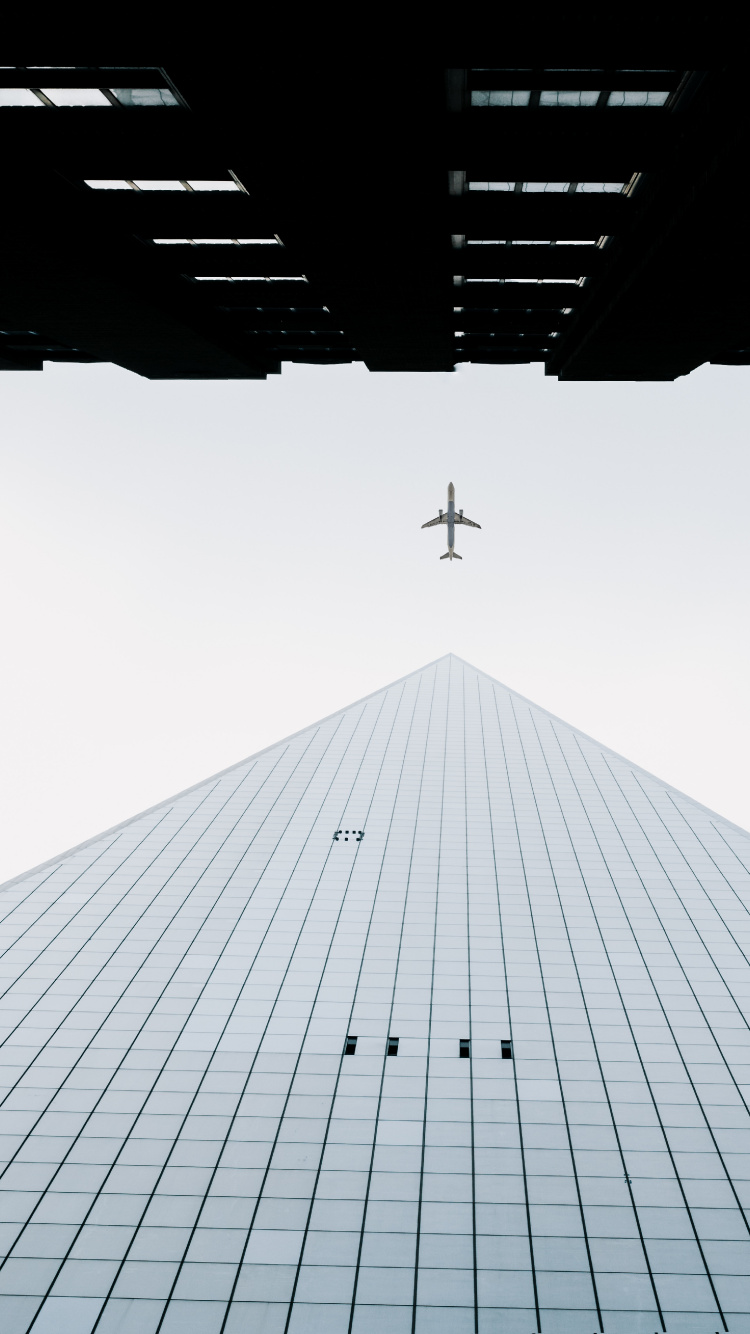 Airplane Flying Over The Building. Wallpaper in 750x1334 Resolution