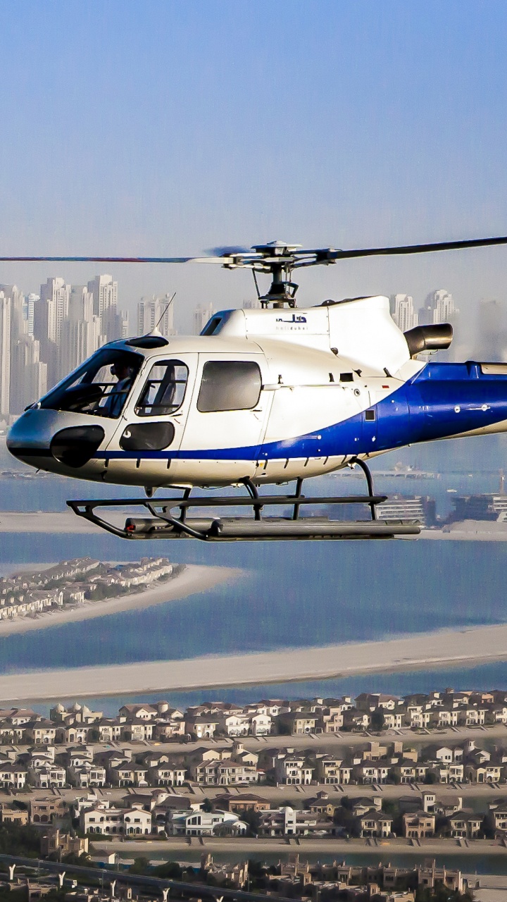 Hélicoptère Blanc et Bleu Survolant Les Bâtiments de la Ville Pendant la Journée. Wallpaper in 720x1280 Resolution