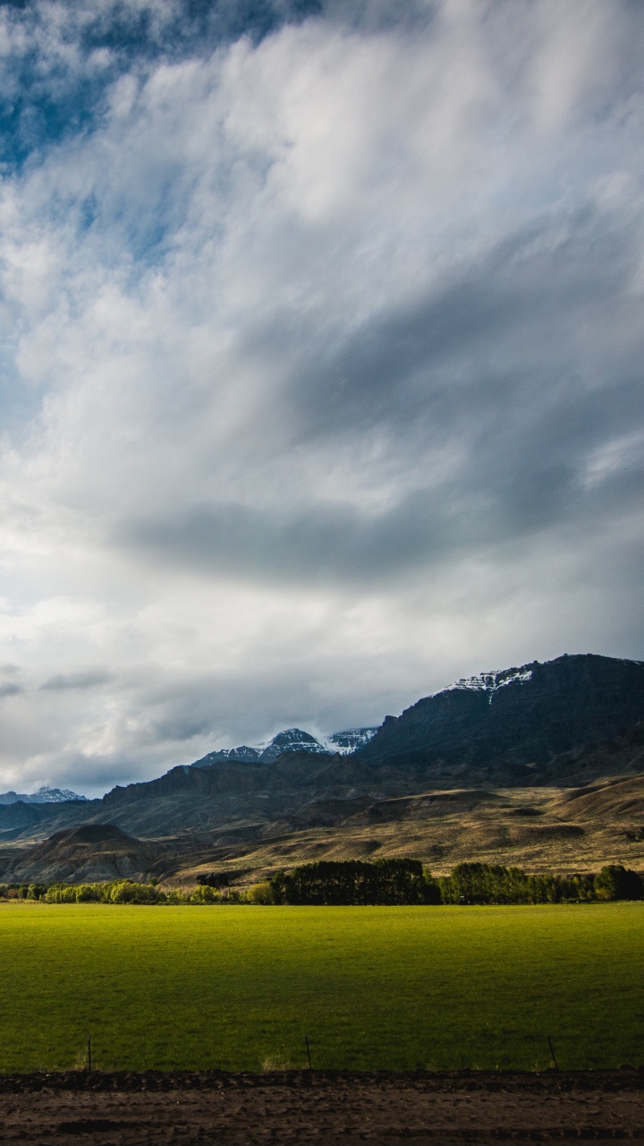 Green Grass Field Near Brown Mountain Under White Clouds and Blue Sky During Daytime. Wallpaper in 720x1280 Resolution