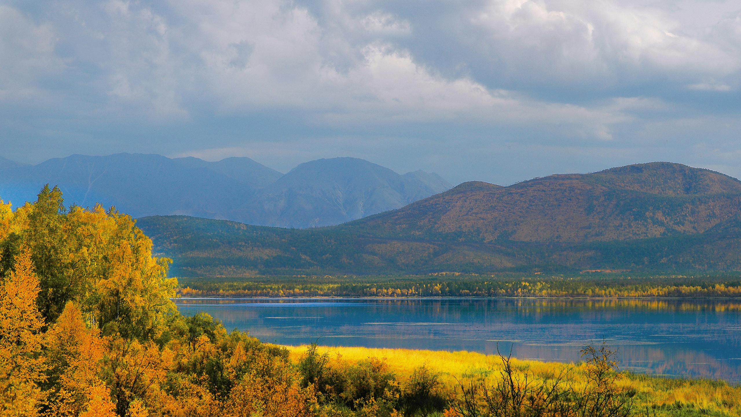 Montañas Verdes Cerca Del Cuerpo de Agua Bajo un Cielo Nublado Durante el Día. Wallpaper in 2560x1440 Resolution