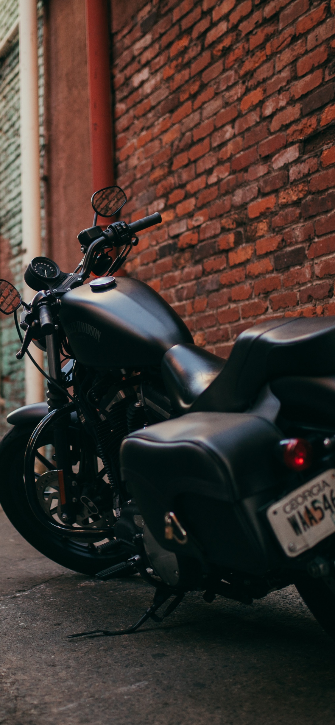 Motocicleta Negra Estacionada Junto a Una Pared de Ladrillo Marrón. Wallpaper in 1125x2436 Resolution
