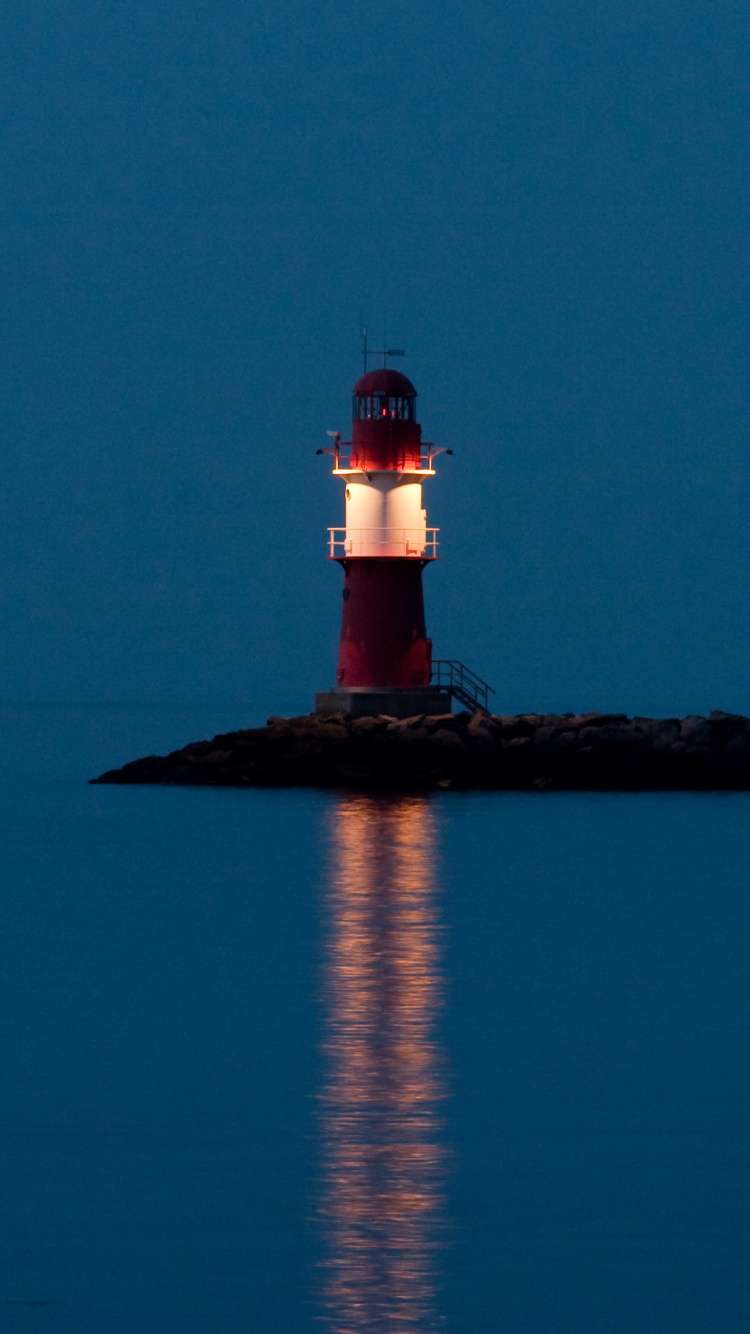 Faro Blanco y Rojo Cerca Del Cuerpo de Agua Durante la Noche.. Wallpaper in 750x1334 Resolution