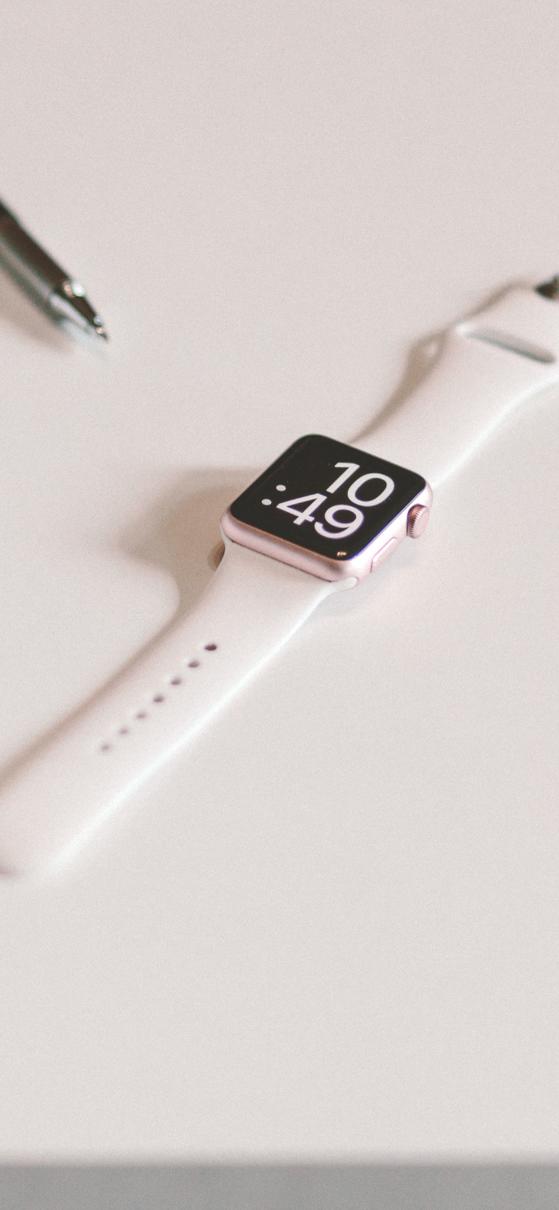 Silver Apple Watch With White Sport Band Beside Black Click Pen. Wallpaper in 1125x2436 Resolution