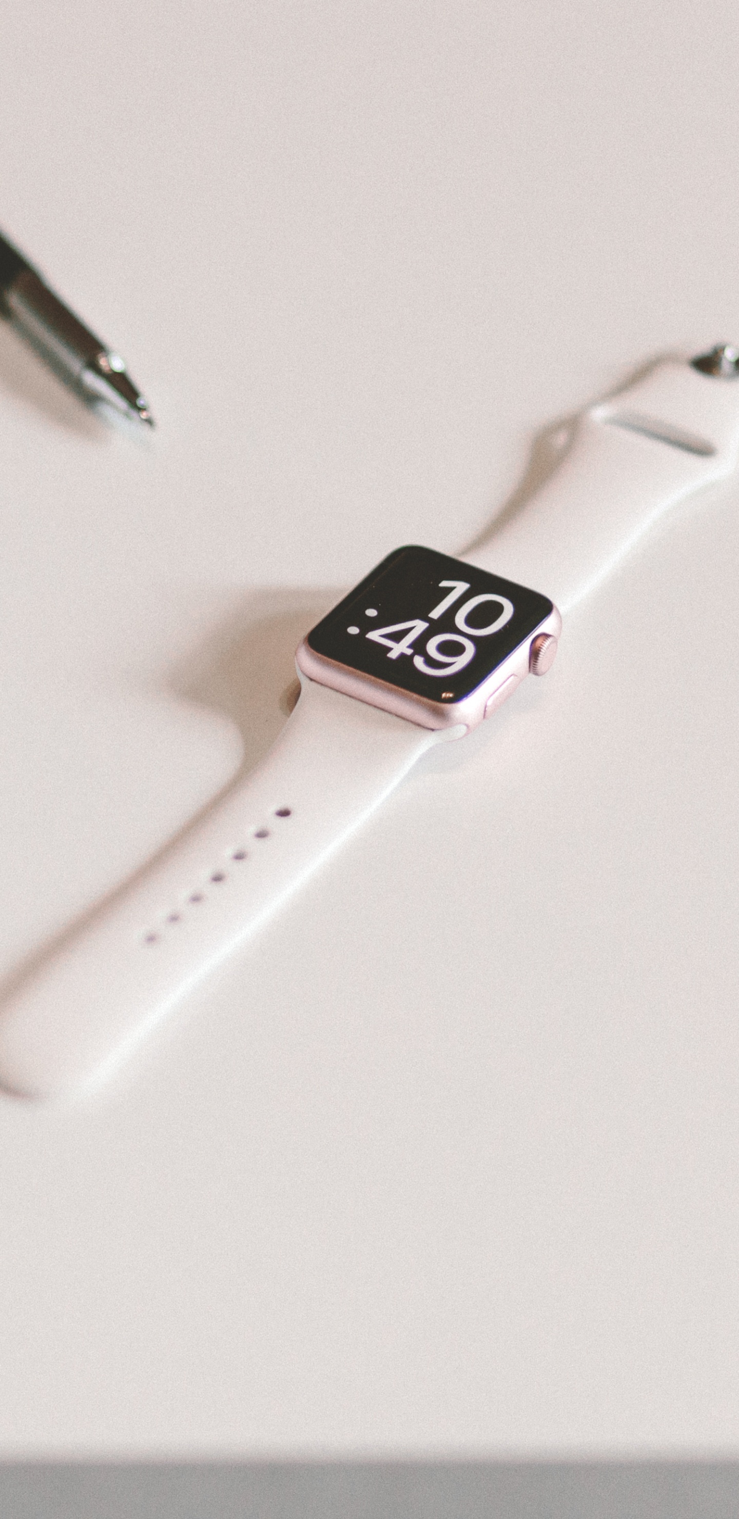 Silver Apple Watch With White Sport Band Beside Black Click Pen. Wallpaper in 1440x2960 Resolution