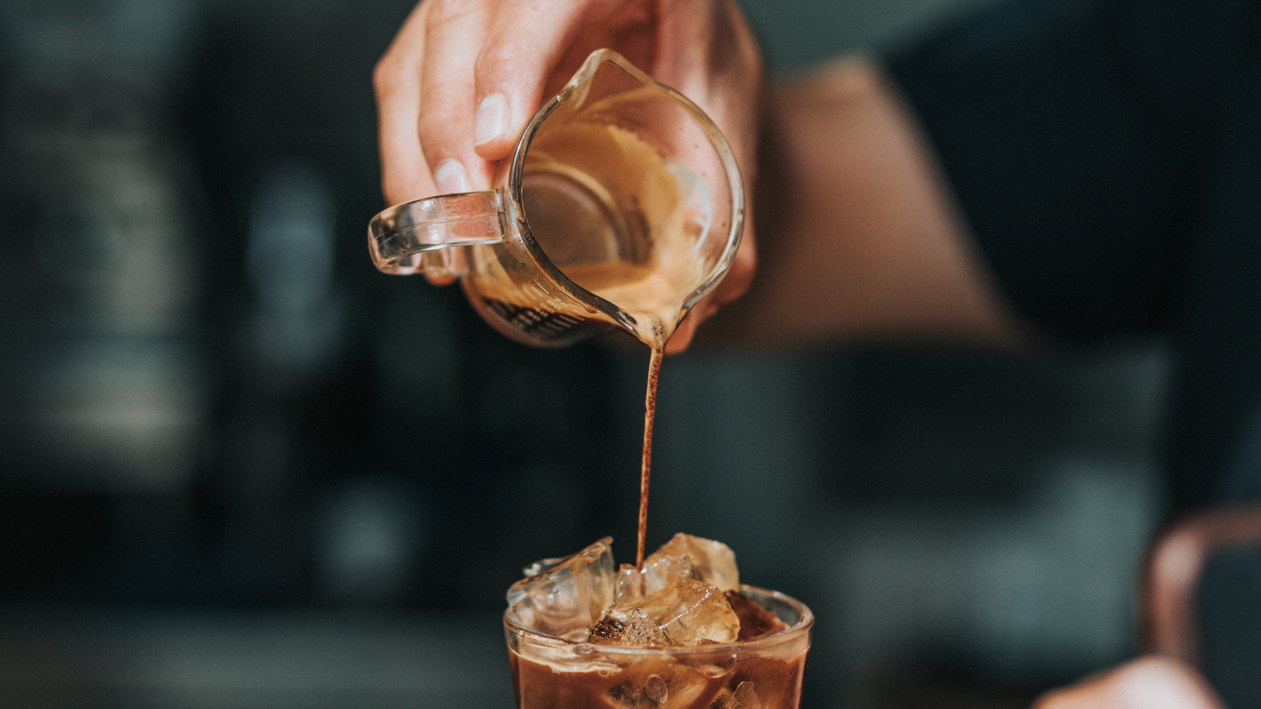 Person Pouring Brown Liquid on Clear Drinking Glass. Wallpaper in 2560x1440 Resolution