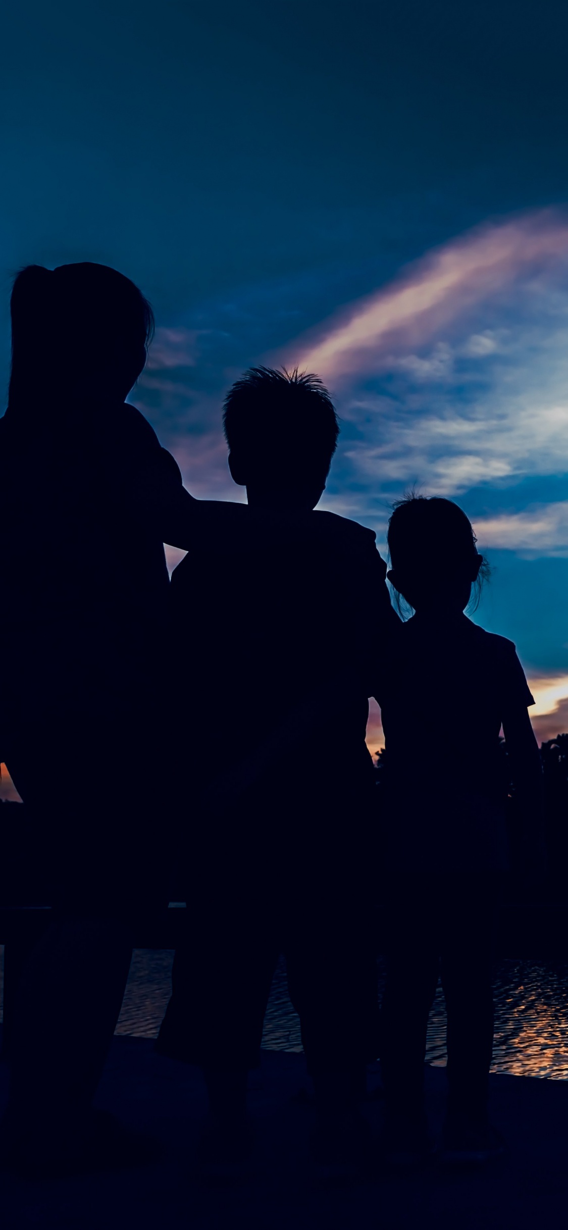 Silhouette of People Standing Near Body of Water During Night Time. Wallpaper in 1125x2436 Resolution