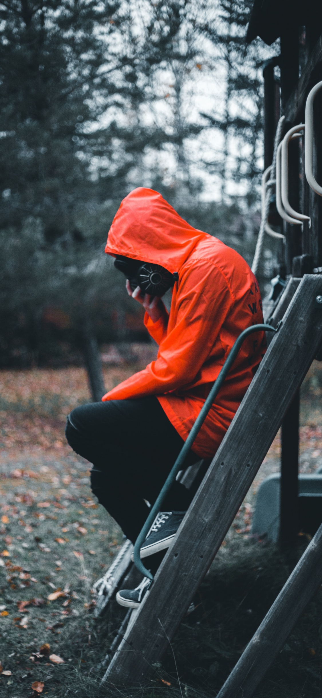 Hombre Con Sudadera Con Capucha Naranja y Pantalón Negro Sentado en la Escalera de Madera Marrón. Wallpaper in 1125x2436 Resolution