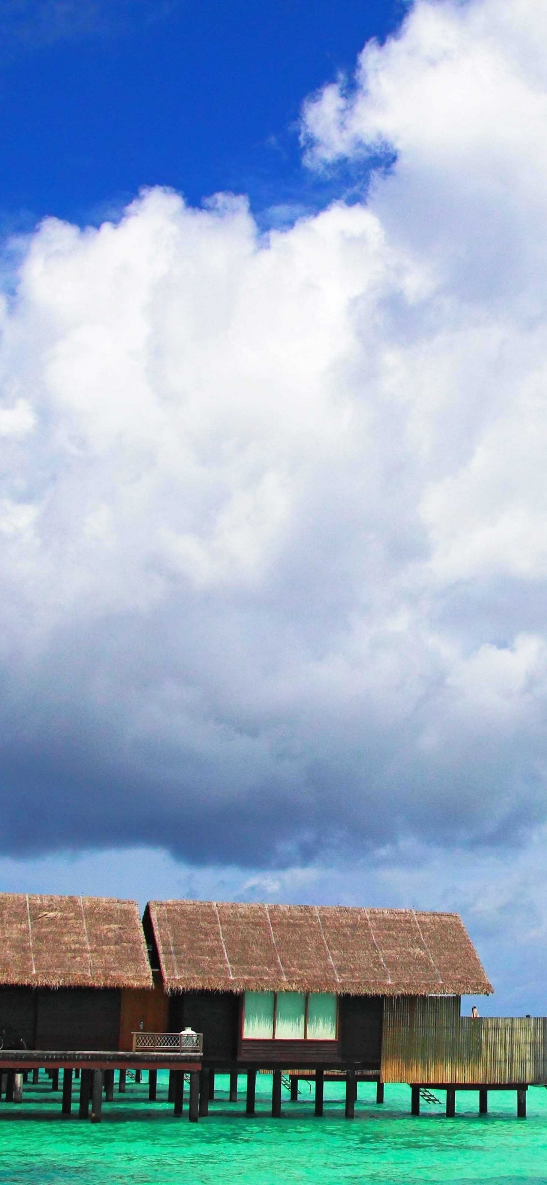 Brown Wooden House on Sea Shore Under White Clouds and Blue Sky During Daytime. Wallpaper in 1125x2436 Resolution