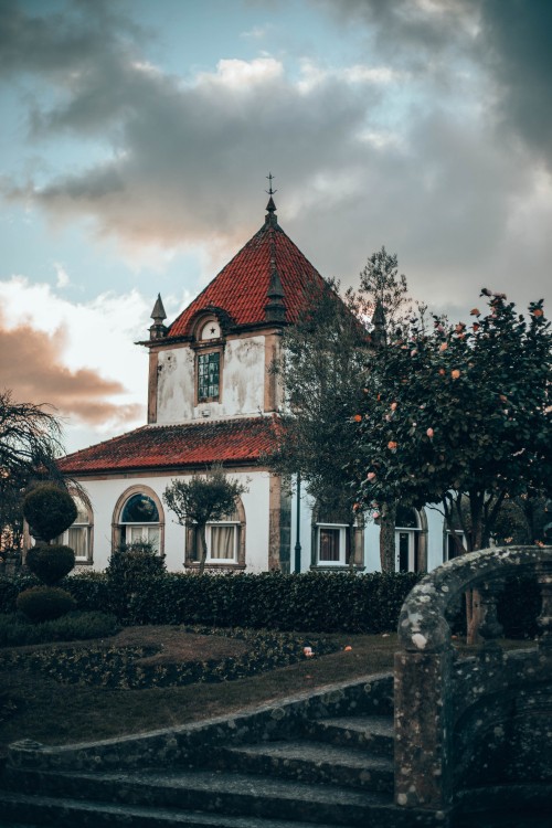 Image red and white concrete building near green trees under white clouds during daytime