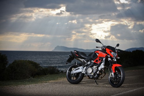 Image black and orange sports bike parked on gray concrete road near body of water during daytime